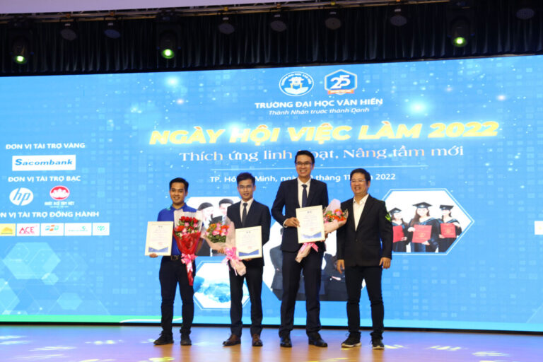 Four men on stage holding certificates and bouquets at a 2022 job fair event in Vietnam