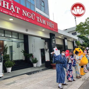 People in yukata pose outside a Japanese language school, with a mascot in the background