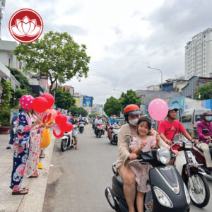People on scooters and sidewalks holding red and pink balloons on a busy city street